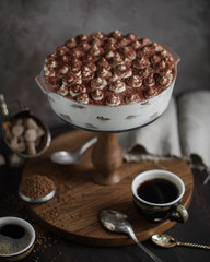 Classic tiramisu cake in a glass baking dish on a high wooden stand. Two cups of strong coffee. Dessert mascarpone with cocoa powder.