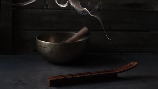 Smoke from aroma stick on dark wooden background with singing bowl