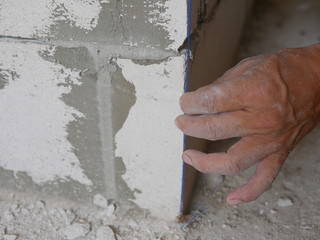 A man's hand holding on a blue string, established by the use of a plumb bob or plummet, used as a vertical reference line for wall in construction
