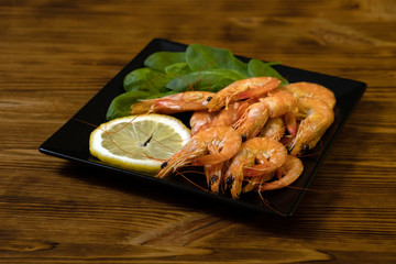 Seafood. Fried roasted shrimps in plate with lemon and greens herbs. Delicious sautéed shrimp on wooden plank, black background