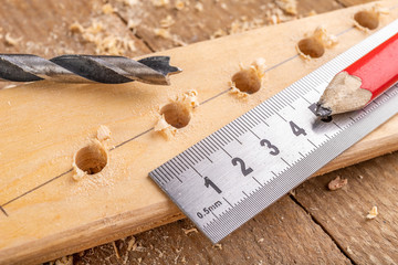 Creating holes with a metal drill in a piece of wood. Metal ruler for measuring the distance...