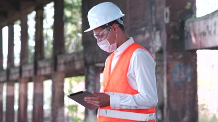 Young engineer man in mask at new job. Electronic data processing on a tablet at a construction site. Lack of confidence in the performance of work duties. - Powered by Adobe