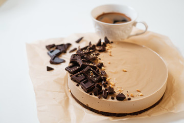 Homemade chocolate cake on parchment paper. Food delivery. Homemade baking. Top view. Delicious tart with chocolate on the white table with cup of coffee.