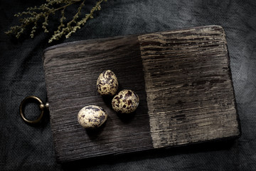 A dark background for a culinary theme is a wooden Board with three quail eggs. Copy space. Flatlay