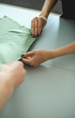 Cropped view of tailor and seamstress holding green fabric on table in workshop 