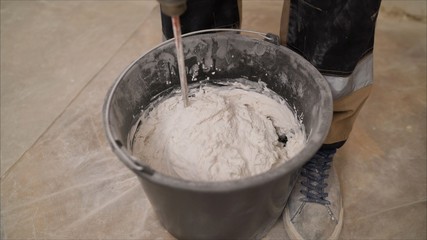 Mix the mixture in a black bucket. Worker mixes a solution in a black bucket. A man mixes a white mixture in a bucket. White substance in a black bucket.