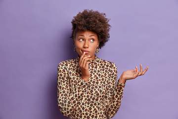 Portrait of confused dark skinned female model dressed in leopard clothing, cannot solve puzzle,...