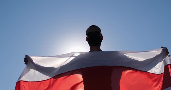 A man spreads the flag of Belarus with his hands on his back. The flag flutters in the wind.