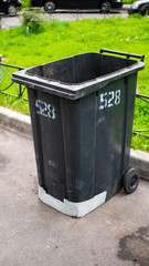 Black plastic garbage collection container on the street with the lid open