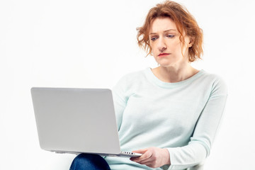 Portrait of a red haired mature woman with serious or puzzled expression on her face with a laptop against white background