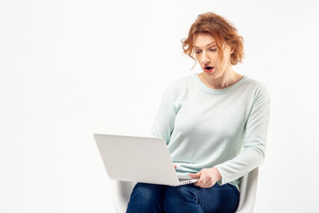 Portrait of a red haired mature woman with surprised expression on her face with a laptop against white background