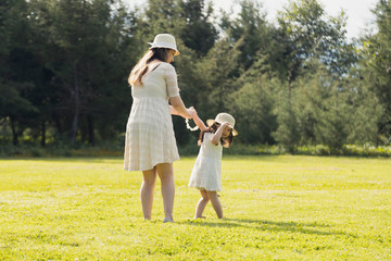 Young Hispanic mother with her little daughter walking hand in hand - mother and daughter taking a walk through a green field in the afternoon - mother and daughter traveling