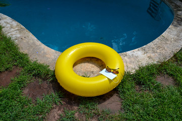 Blue face mask for protection against the Corona Virus (COVID-19), sunglasses laying on a pool mat beside a swimming pool during coronavirus worldwide pandemic holidays