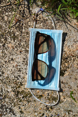 Blue face mask for protection against the Corona Virus (COVID-19), sunglasses laying beside a swimming pool during coronavirus worldwide pandemic holidays