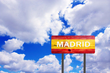 Sign on wooden plate indicating direction to Madrid with view of cloudy sky