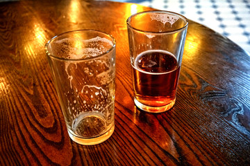 Two glasses of beer, one empty and one full, on wooden table