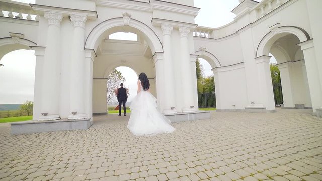 bride in a wedding dress runs to groom at sunset or sunrise against the backdrop of beautiful architecture. Slow motion. Europe. Fashion young woman goes to her husband hugs him and kisses Slow motion