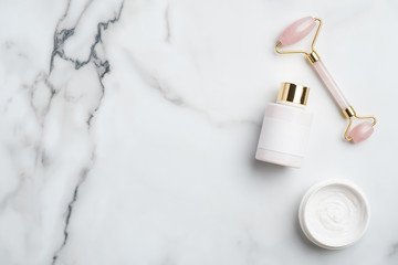 Face skin care concept. Quartz facial massager, lotion bottle, moisturizer cream on marble desk....