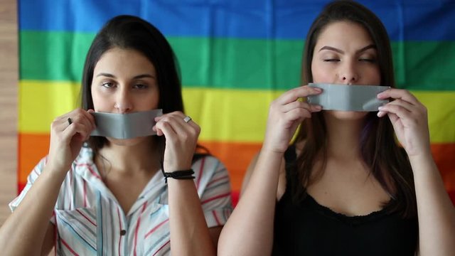 Two women looking at camera taping duct tape in mouth. LGBT censorship concept