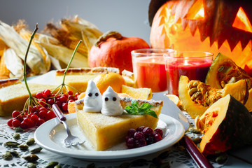 Sweet homemade halloween pumpkin cake with leaf of mint and small ghosts on white plate closeup. Candles and Jack-o-lantern on background. Traditional holiday food