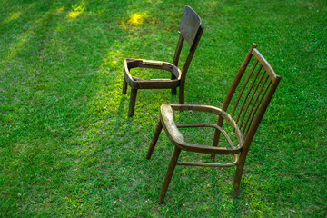 Two old wooden chairs without a seat stand on the green grass in the garden
