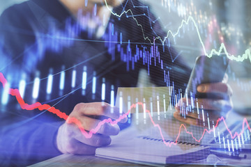 Double exposure of man's hands holding and using a phone and financial graph drawing. Analysis concept.