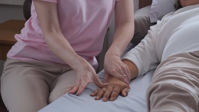 two age generation are happy on bed at home on vacation. The eldest daughter was giving an elderly mother a hand massage while she was asleep to relax, family time concept.