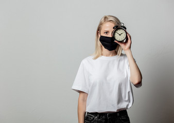 Fototapeta premium Woman in white t-shirt and black face mask with alarm clock on white background