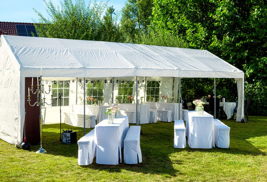 White tent with wedding table setting decorated with fresh flowers , champagne coolers, and decorative glasses for wedding party in a garden