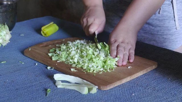 Middle age woman cuts cabbage on wooden board on table