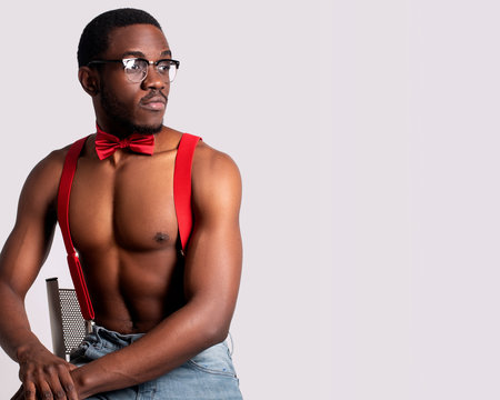 Topless African American model wearing suspenders, red bowtie and blue jeans
