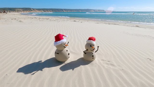 Two Sandy Christmas Snowmen are celebrating Christmas on a beautiful beach, zoom out