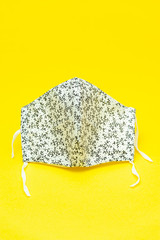 Pandemic COVID-19 - Floral pattern (white and black color) DIY fabric face mask for protection against coronavirus and other infectious diseases. Isolated on yellow background.  copy space.