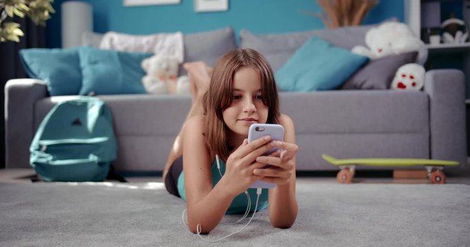 Relaxed female teenager lying on floor and using modern smartphone during leisure time. Young lady in casual outfit spending free time online on gadget.