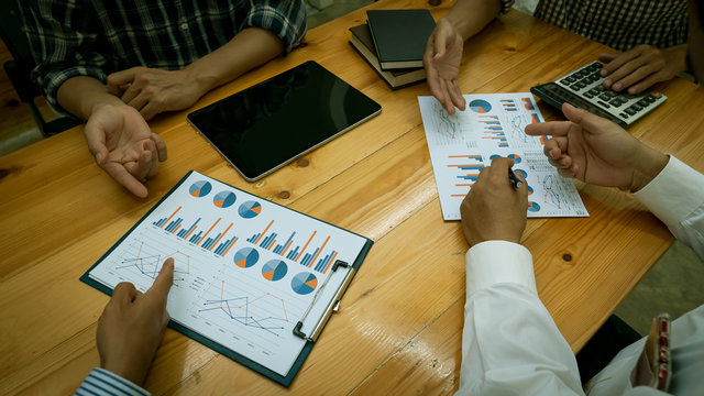 Many businessmen who point to the graph and chat in an office with a laptop on their desk.