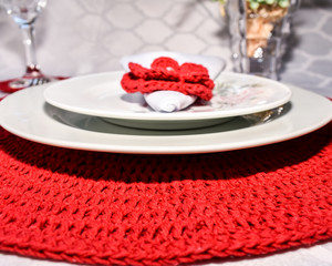 Red handmade crochet sousplat, white plate, white dessert plate and red crochet flower.