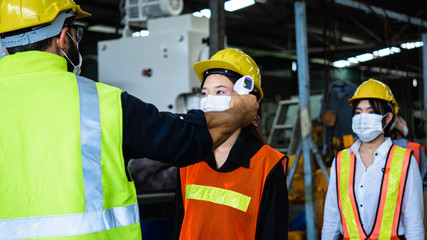 Industrial worker and engineer stand in line to check flu with infrared thermometer before enter to...