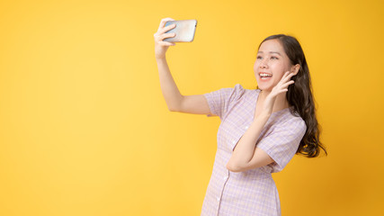 Asian beautiful girl taking selfie, Thai woman take photo by phone in studio on yellow background