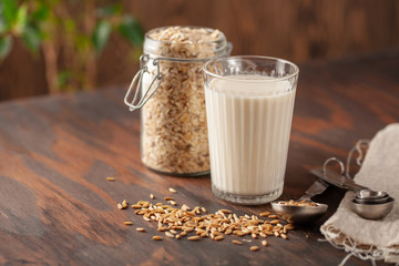 Vegan oat milk, non dairy alternative milk in a glass. Oat flakes  on wooden table.