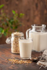 Vegan oat milk, non dairy alternative milk in a glass. Oat flakes  on wooden table.