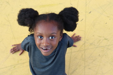 Arial shot of happy black little girl sitting on yellow background