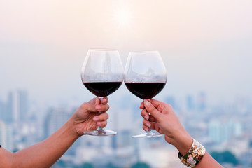 Hand of a lover's dinner is celebrated with red wine at a restaurant in a romantic atmosphere. Sunset and modern city background