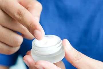 Hand of man holding moisturizer cream and serum. he applying a facial cream , essential , oil , lotion and body cream for skin care, close up view and blur background. Beauty and Healthy Concept.