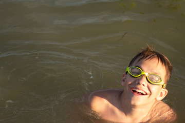 A 10-year-old boy is swimming and having fun in the sea near the shore in green swimming goggles.