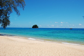熱帯のリゾート地の青い海に浮かぶ小島と小船と手前の木