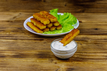 Fried fish fingers on a plate with lettuce and tartar sauce on wooden table