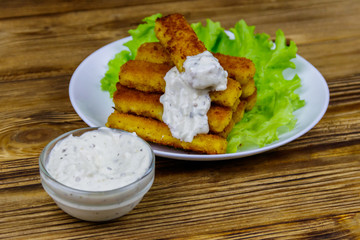 Fried fish fingers on a plate with lettuce and tartar sauce on wooden table
