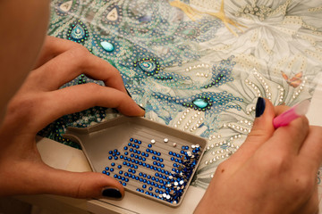 Diamond painting embroidery craft. Acrylic rhinestones and hand holding a pen. Closeup, selective...