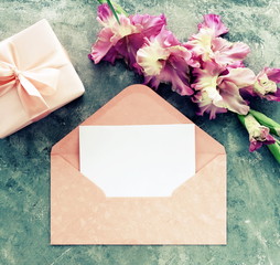 greeting cards mockup template, invitations blank, envelope , pink gladiolus flower, gift box top view on gray paint textured background toned. Flat lay, top view, copy space