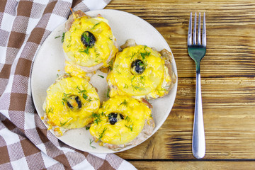 Pieces of baked pork with pineapple, cheese and olive on a wooden table. Top view